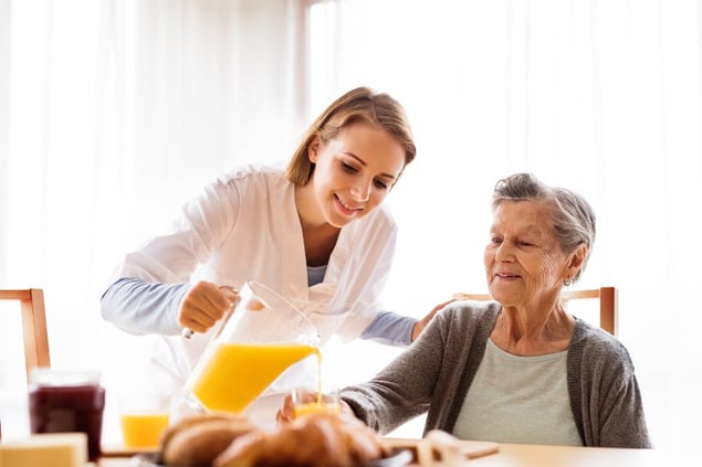 A nurse pouring a pitcher of orange juice.