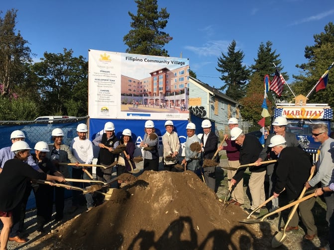 People in hardhats dig into a mound of dirt to break ground on the new Filipino Community Village.