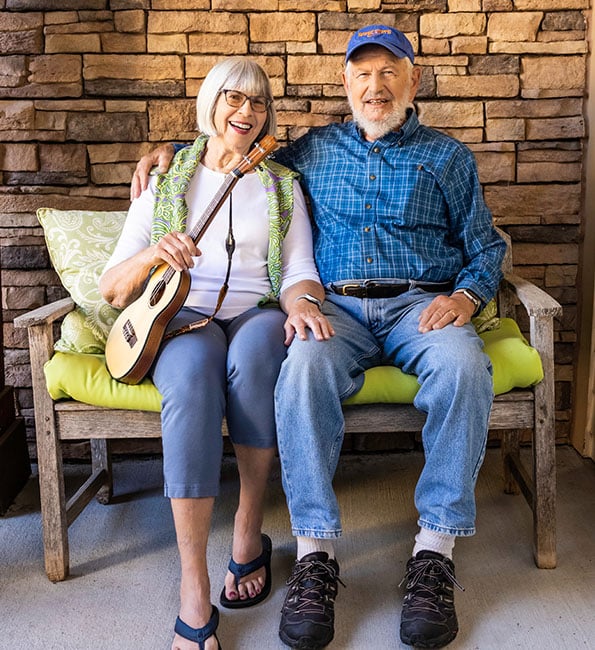 Tom and Mary, who is holding a ukulele, sitting on an outdoor bench