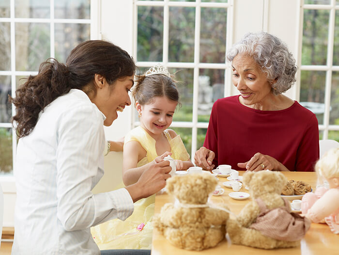 Mother and grandmother share a tea party with young girl. 